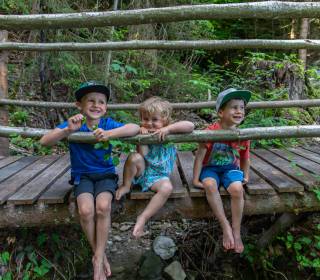 Kinder sitzen auf Waldbrücke und lassen die Beine baumeln