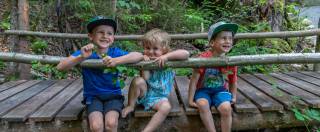 Kinder sitzen auf Waldbrücke und lassen die Beine baumeln