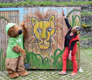 Frau mit Maskottchen Toni vor Grafikwand
