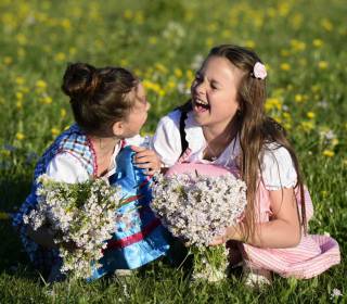 Zwei Mädchen sitzen in einer Blumenwiese und lachen